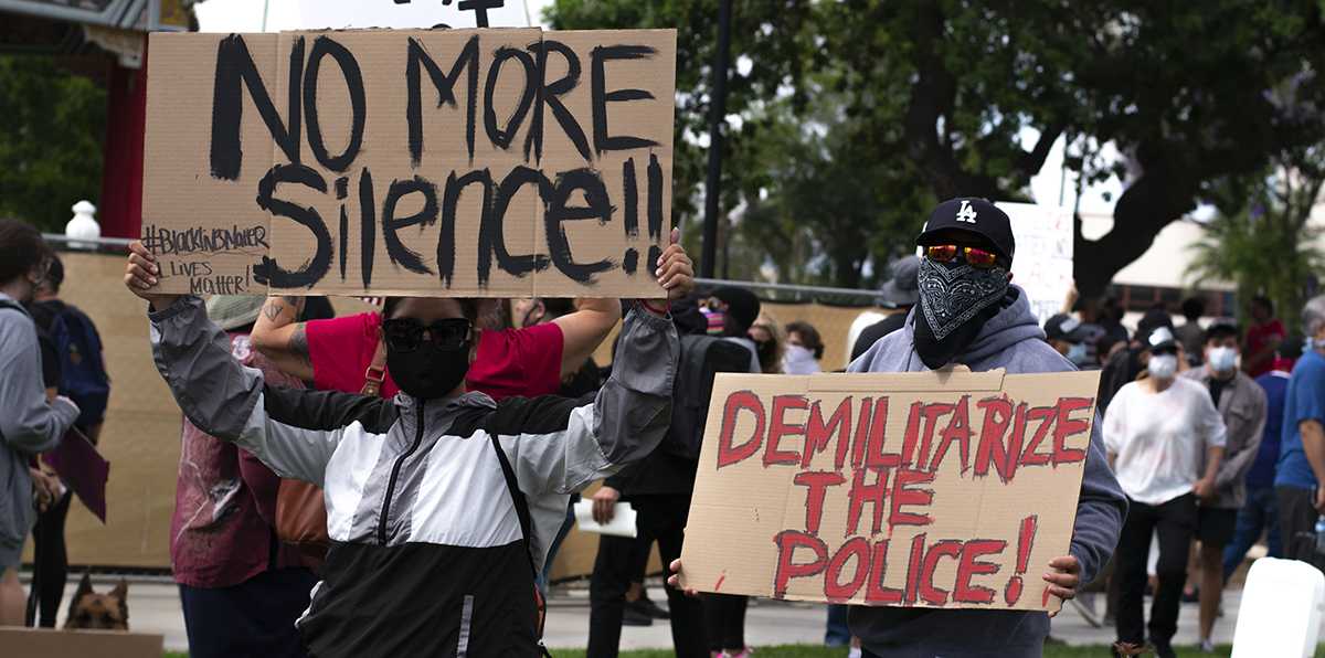 Two demonstrators hold signs calling to demilitarize the police and for no more silence at the Black Lives Matter Protest in Downtown Riverside June 1. (Jonathan Ramirez | Viewpoints)