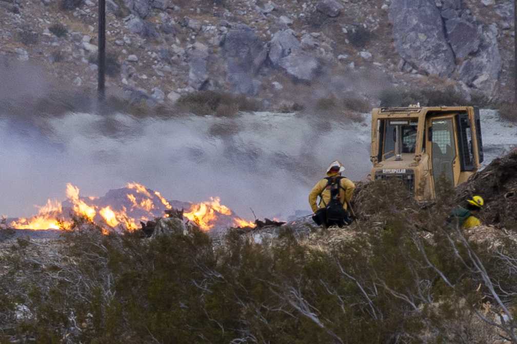 A mirage from the heat of the Kellogg Fire distorts the background as a a heavey equipment operator buldozes a fire break around the 100-foot pile of mulch which ingnited Nov.8, 2020 in North Palm Springs.  Photo by Joyce Nugent/Viewpoints