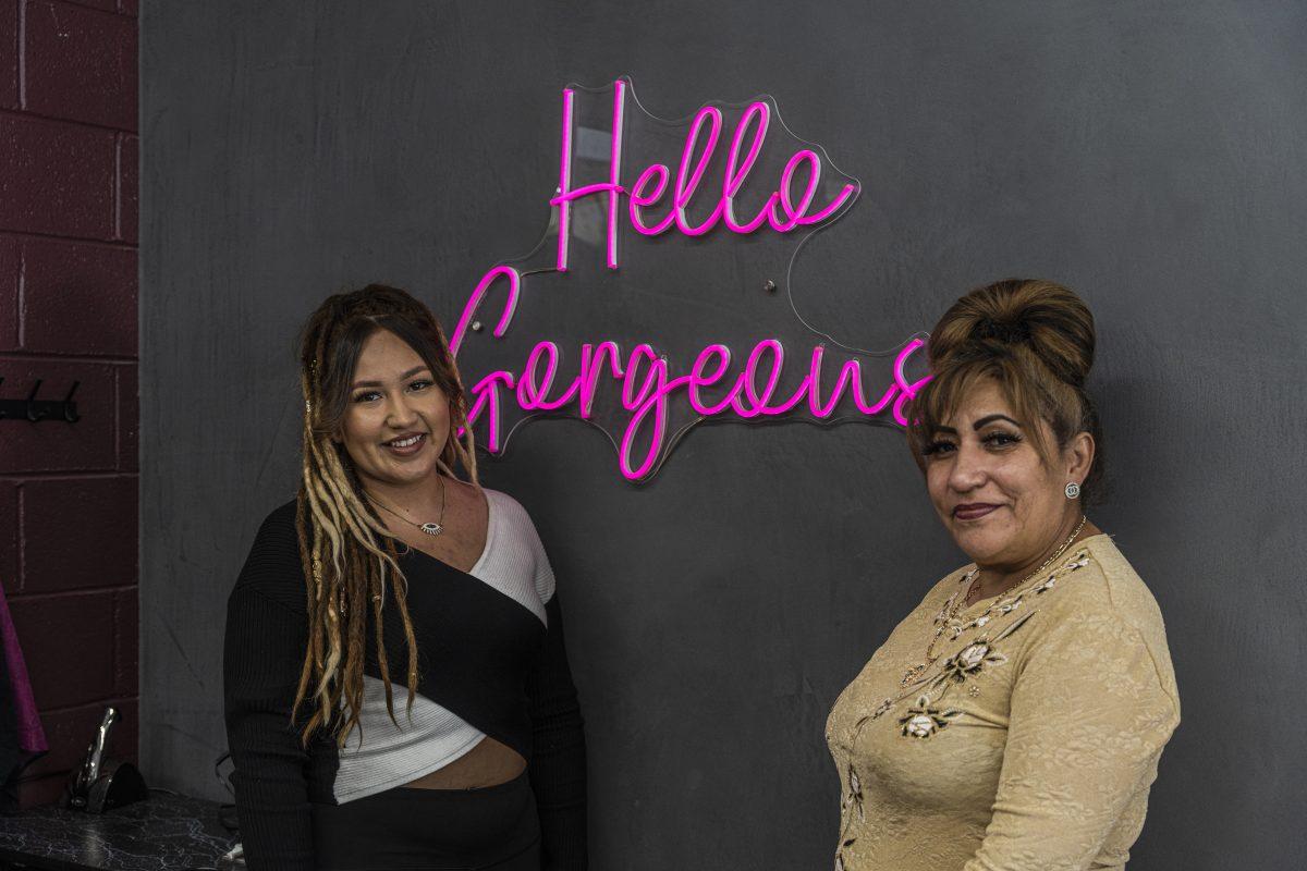 Mother-daughter duo Elia Martinez and Elia Georgette Montes Martinez, stand below a neon sign that says "Hello Gorgeous" in their salon, Magic Scissors. (Stephen Day | Viewpoints)