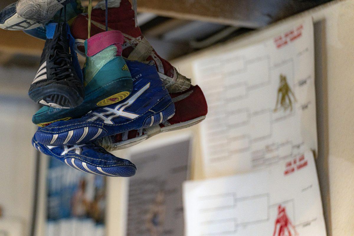 A collection of wrestling shoes from various members of the family hang in a garage with tournament brackets hanging behind them. Photo by Stephen Day, Viewpoints.